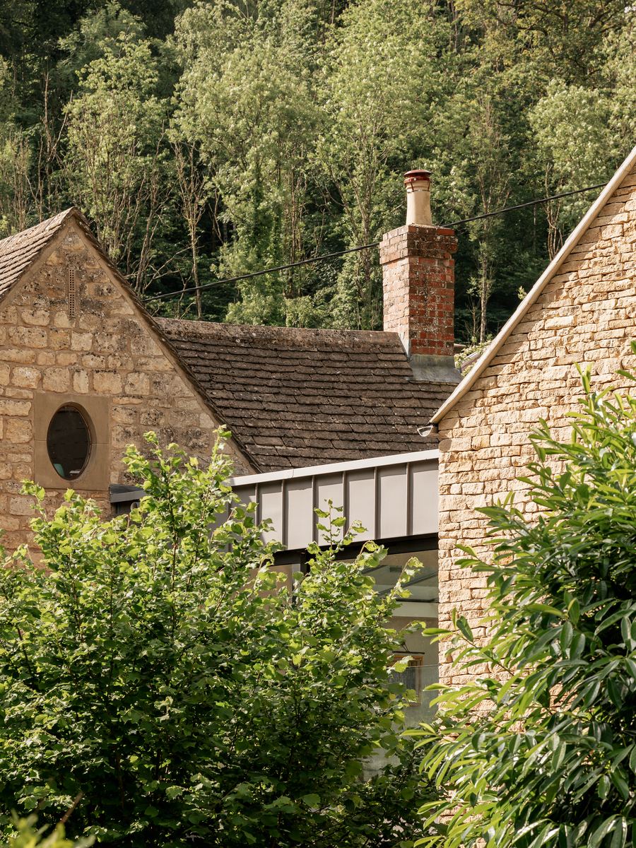 Cotswold Cottage Extension zinc-clad glazed link between the historic stone cottage and new gable, wooded hillside beyond